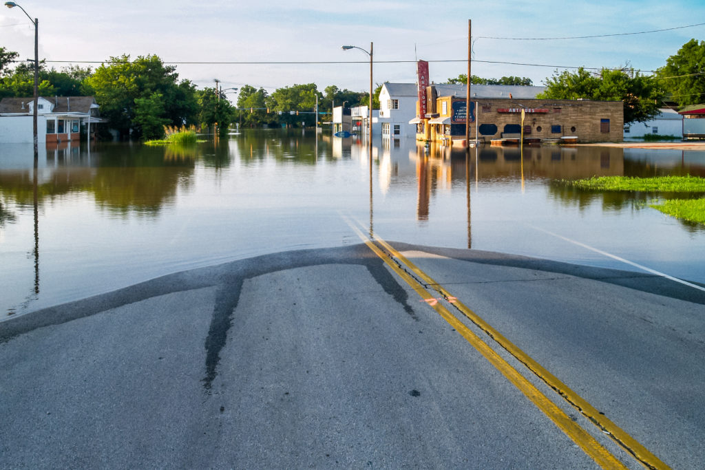 Gives a picture of a common flood. A low level area of a small town is completely submerged in water, including a road, several buildings and homes. 